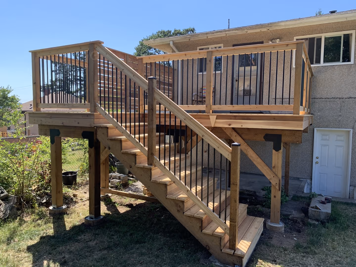 Raised backyard wooden deck with stairs and black metal railings attached to a house.