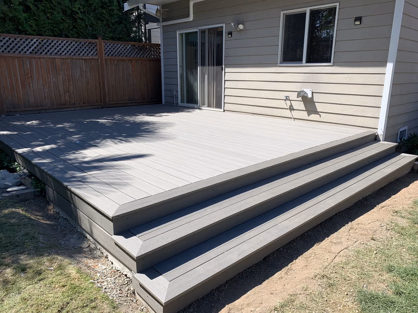 Backyard gray composite deck with three wide steps and a sliding door