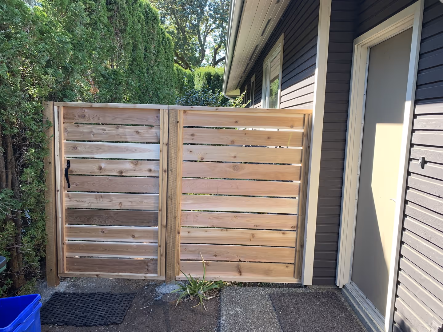 Cedar horizontal-slat side yard gate next to a gray house and tall hedge