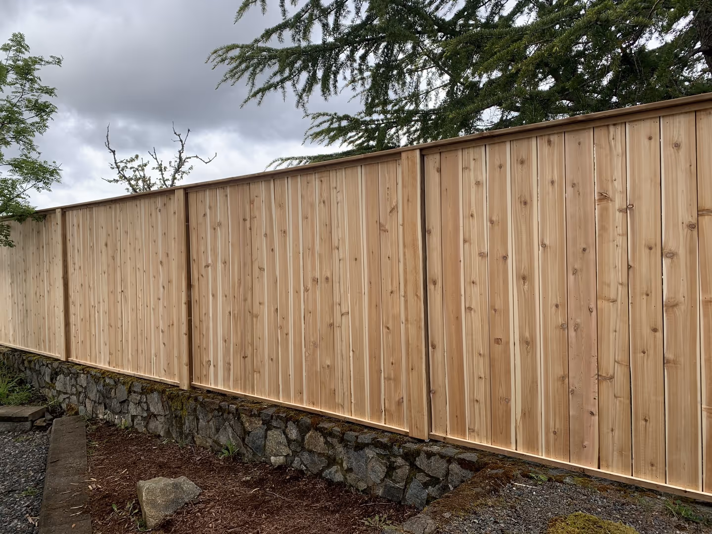 Cedar privacy fence atop a stone retaining wall under cloudy sky