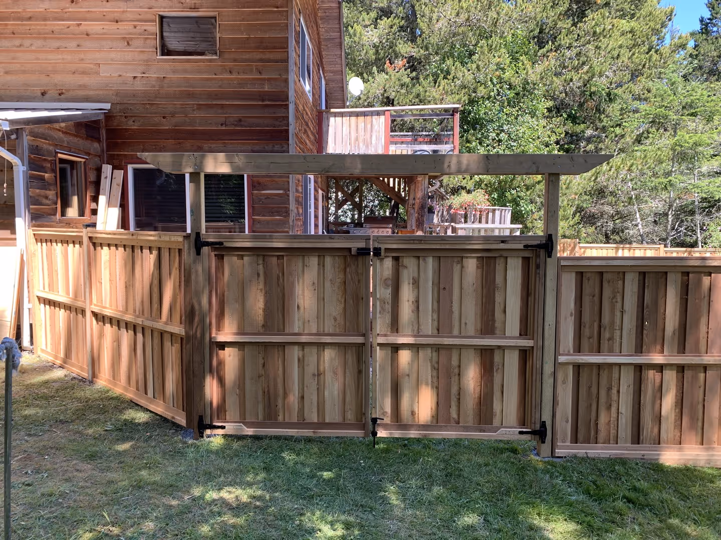 Cedar privacy fence with double gate and overhead awning beside a wooden house.