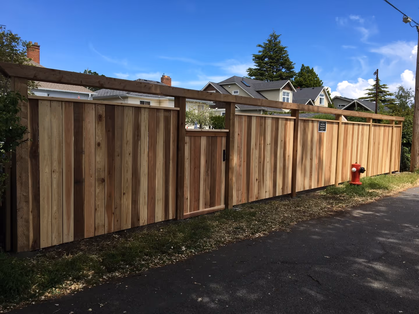 Cedar privacy fence with gate along a residential street, red fire hydrant in front.