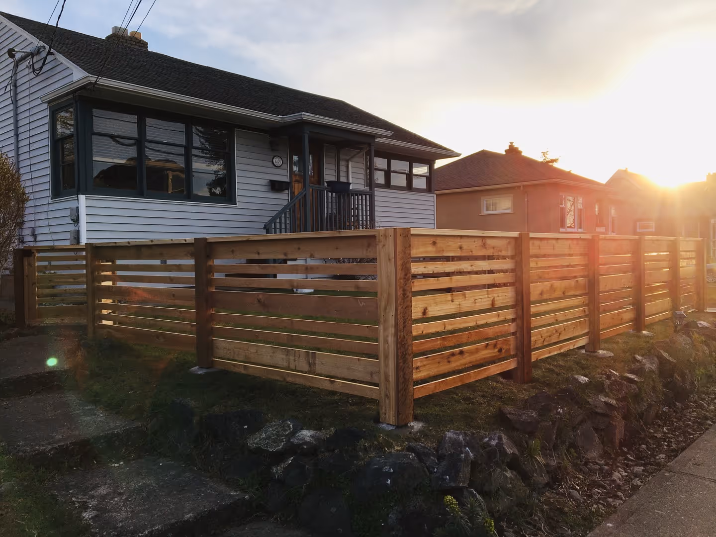 Horizontal slat wood fence around a corner-lot house at sunset