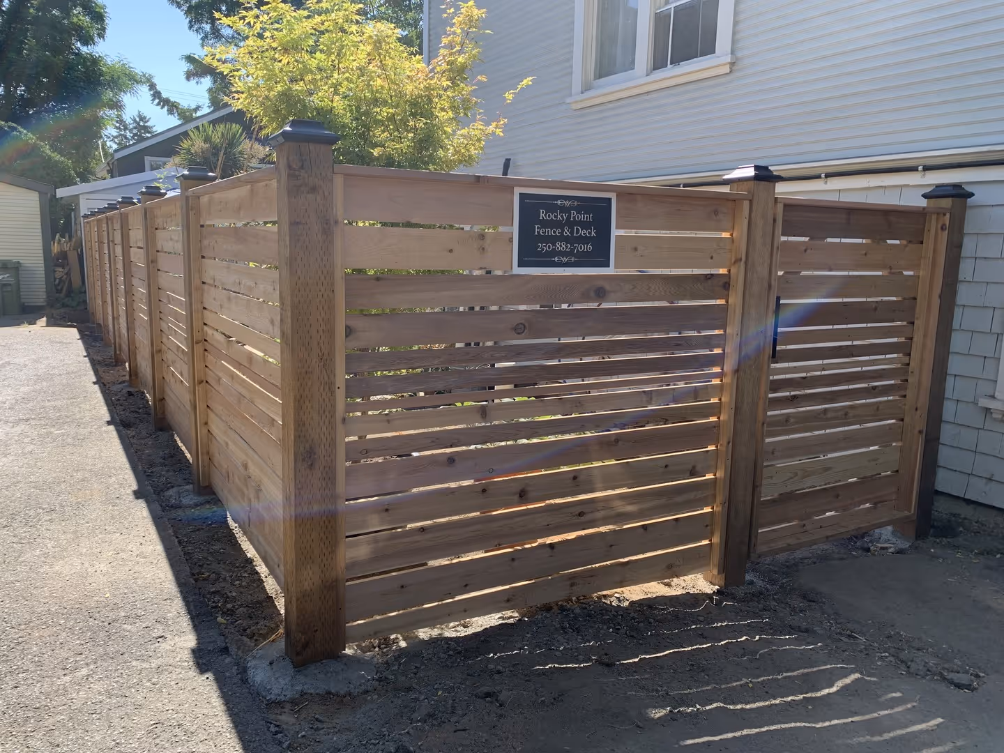 Horizontal wood slat privacy fence with post caps and a Rocky Point Fence & Deck sign.