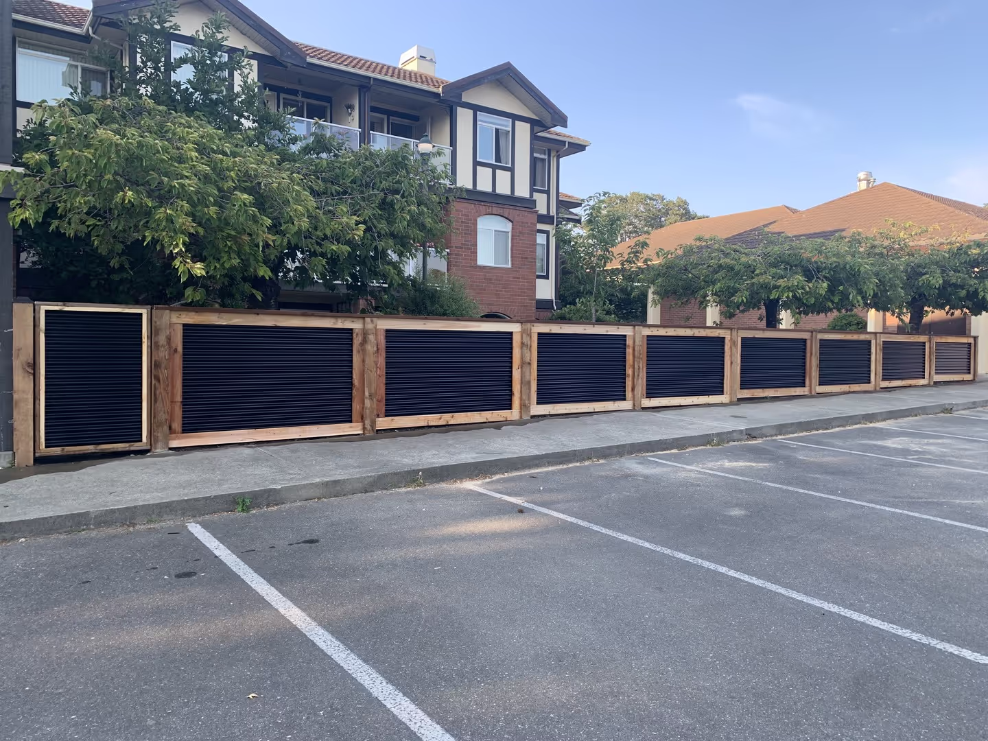 New wood privacy fence with black slats along an empty parking lot at an apartment complex