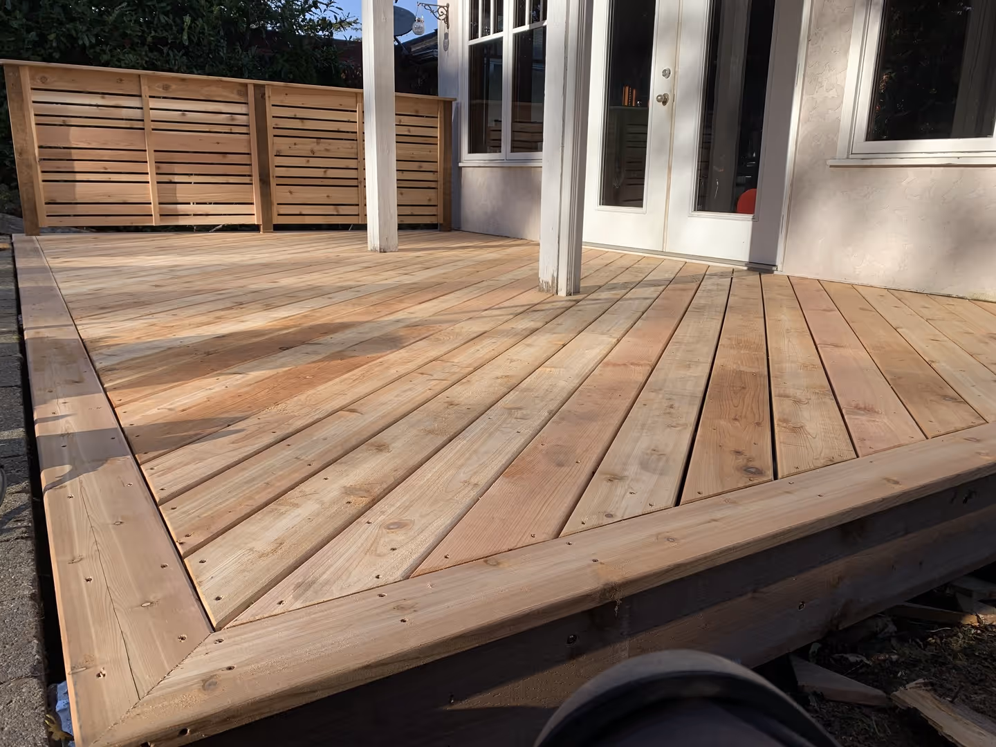 Newly built wooden deck with diagonal boards and privacy screen by French doors.
