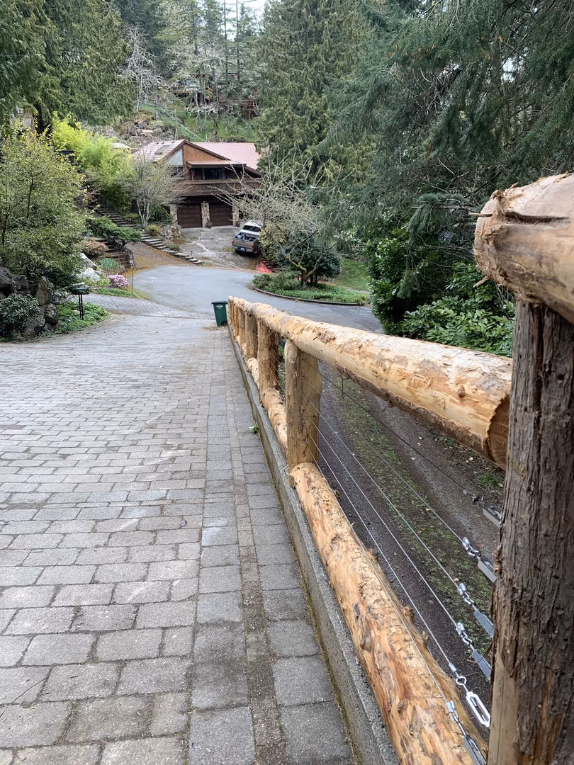 Rustic log railing beside a paver driveway leading to a forest cabin.