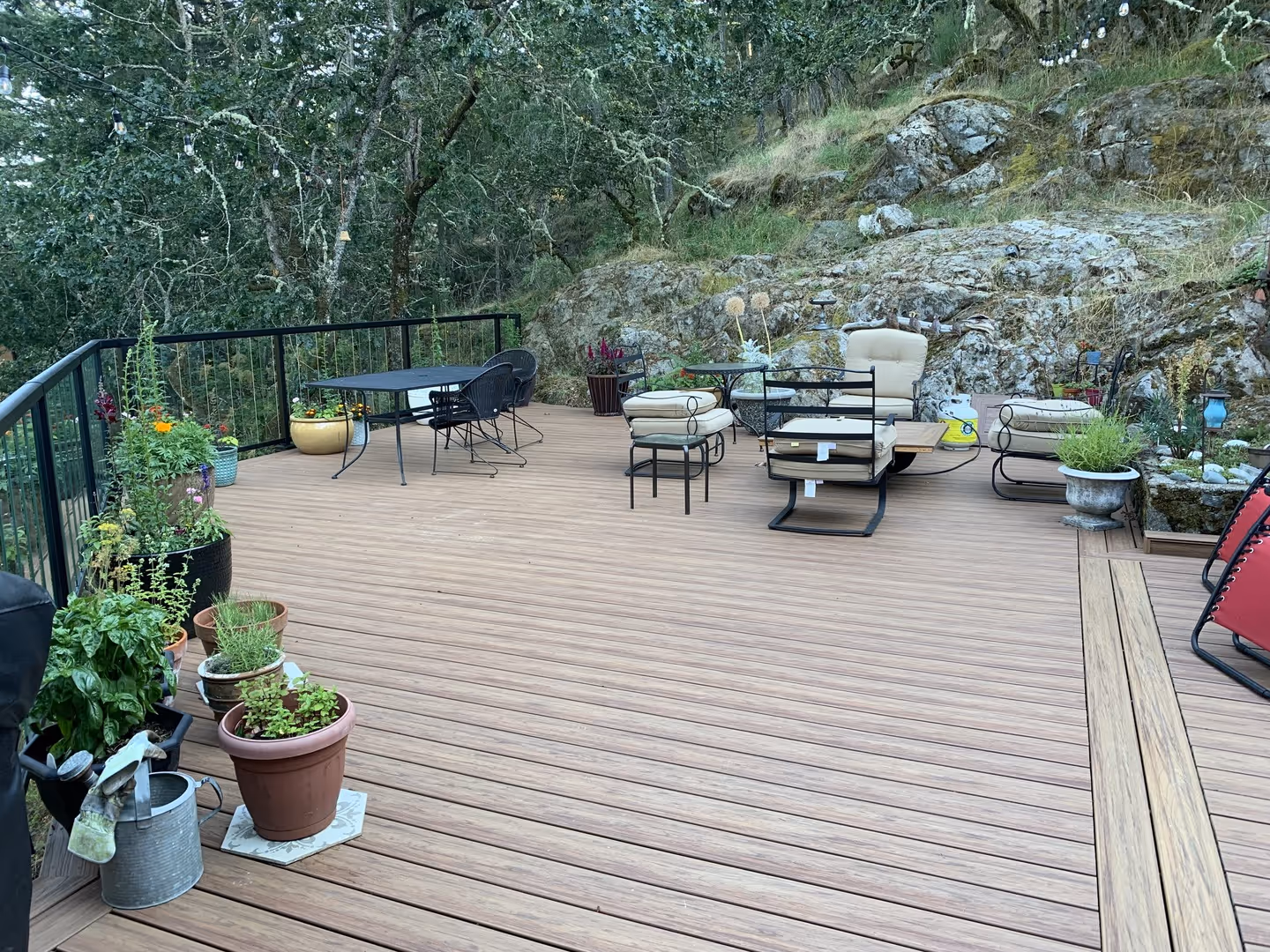 Spacious backyard deck with patio seating and potted plants overlooking a rocky, wooded hillside.