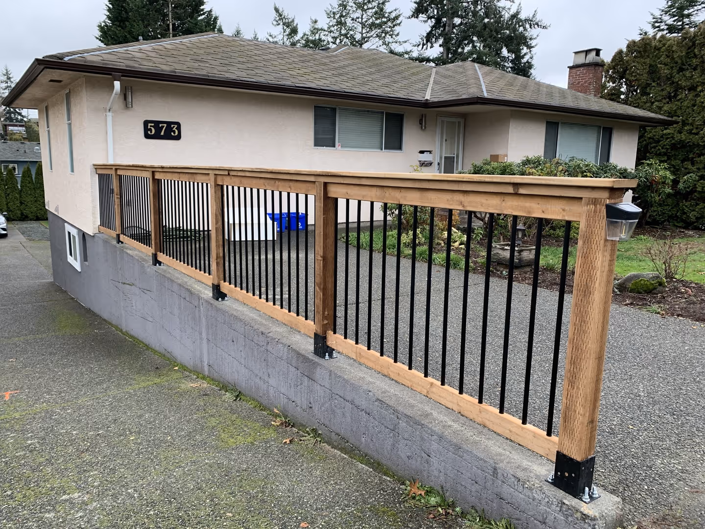 Wood and metal railing on a concrete retaining wall in front of a single-story house.