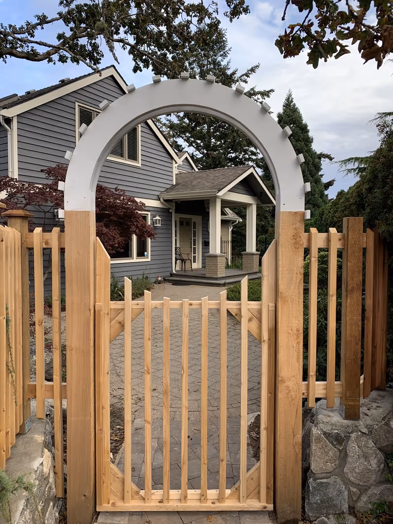 Wooden arched garden gate opening to a gray house with a front porch