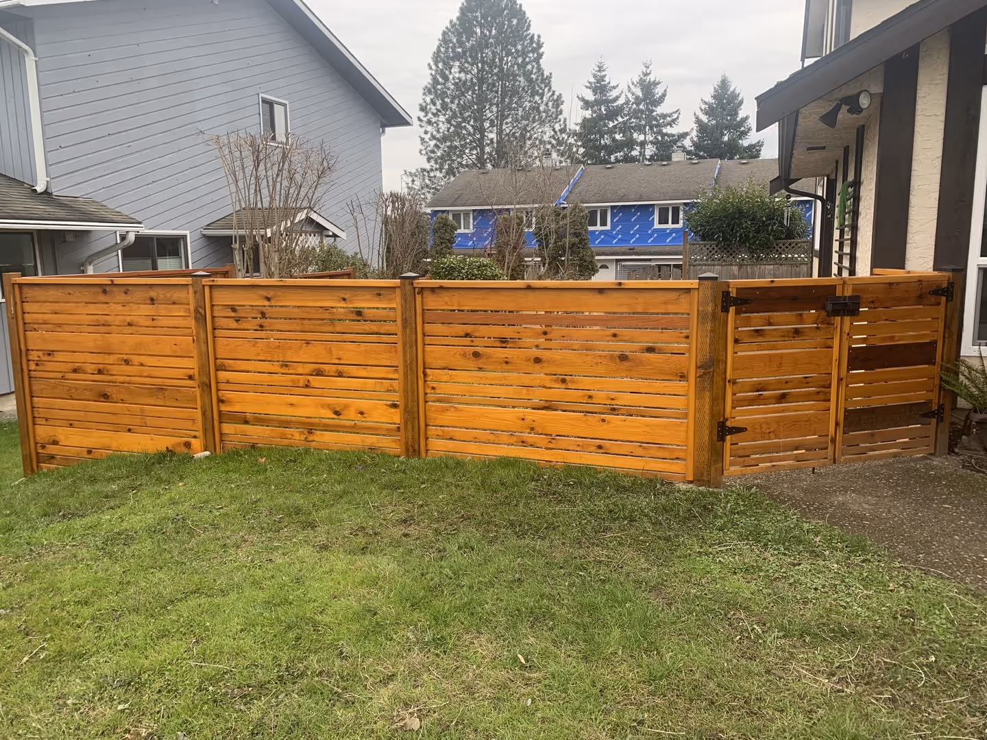 Wooden horizontal privacy fence with gate along a backyard lawn.